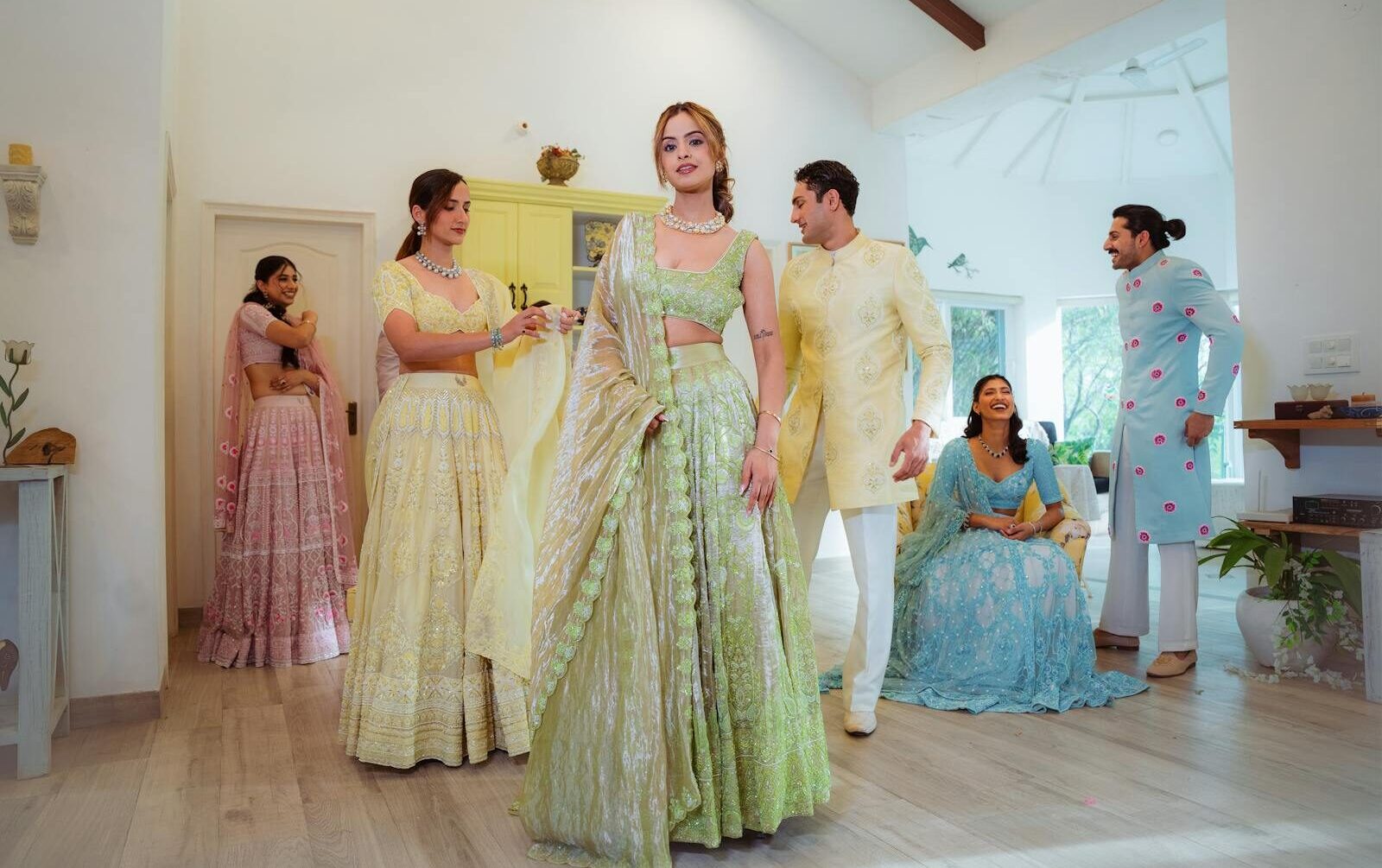 A group of adults in vibrant traditional Indian attire gathered indoors in a well-lit room.